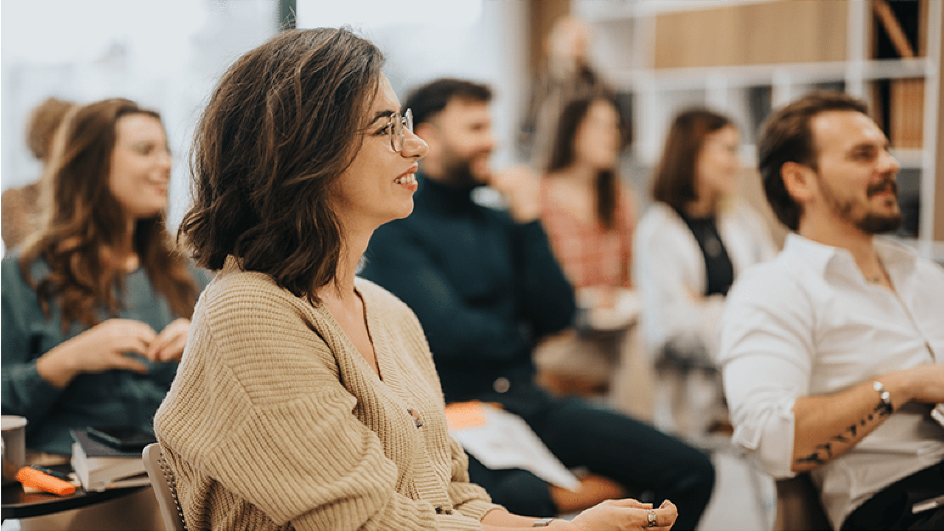 Kobieta siedząca na tle grupy prawdopodobnie słuchaczy