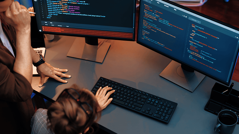 Dwie osoby siedzące przy dwóch ekranach